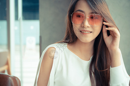 在室内时尚一种美丽的亚洲女穿着太阳眼镜坐在咖啡店里并坐在咖啡厅里图片