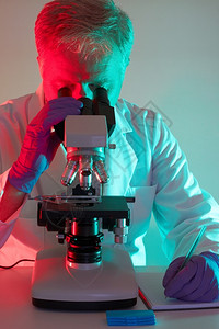 药物坐着医学专业科家通过显微镜进行观察在职的图片