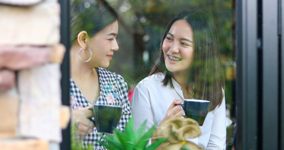 女两个亚裔妇喝咖啡和两个开心愉快的女人在咖啡馆闲聊女士休息图片