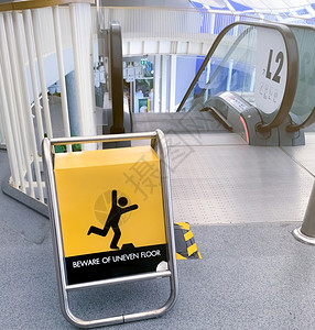 商场营业通知小心黄板在购物商场扶梯前的黄色上发出不均匀的地板警告标志注意在黎晓扶梯安全通知前步行道安全方面发出的不均匀地面警告信号木板走道内背景
