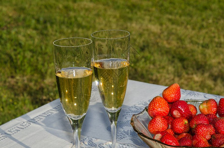 外部金的坐在花园桌边有两杯酒和一碗新鲜草莓浆果图片