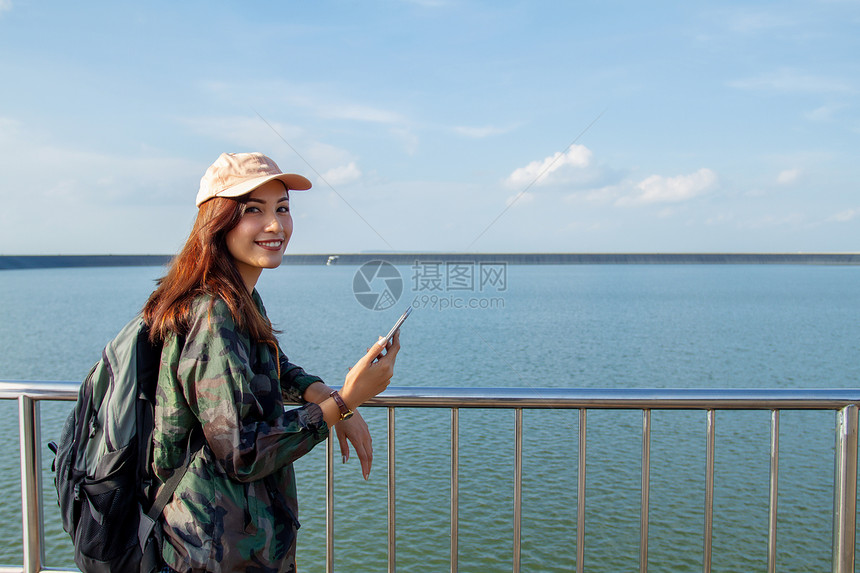 背着明亮包的亚洲女在背景山上的旅游行者背后看使用智能手机的女从后面看图景快乐的亚洲人太阳图片