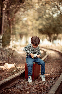 手拿相机的小男孩坐在手提箱上图片