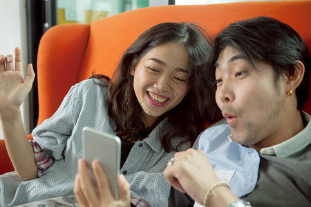 年轻亚洲男女在寻找智能电话屏幕时的快乐情绪笑声惊喜幸福移动的图片