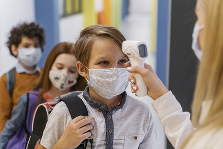 体感温度女孩教师用医疗面具检查学生温度校的体课堂注册背景