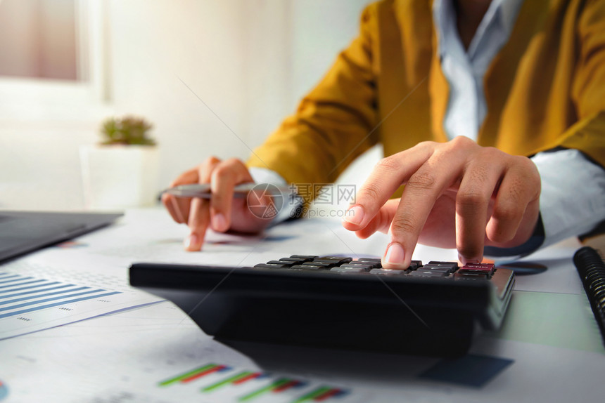 数据桌子利用计算器和笔记本电脑分析财务在办公桌工作的女商人收入图片