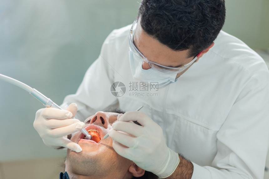 健康诊所成人男牙医对40岁病人进行卫生治疗的照片男牙医为一名40岁的病人提供卫生治疗的相片图片