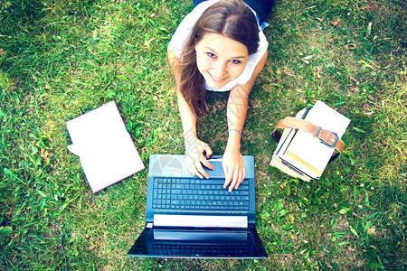 漂亮的女大学生趴在草地上用电脑学习图片