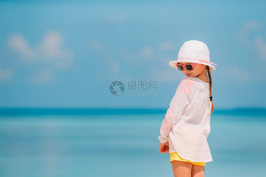 暑假在沙滩上戴帽子的小孩暑假在沙滩上戴着帽子的可爱小女孩在暑假期间穿着帽子户外海岸线支撑图片