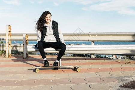 头发随意的青少年女坐在长凳上双脚海面的长板上千禧一代图片