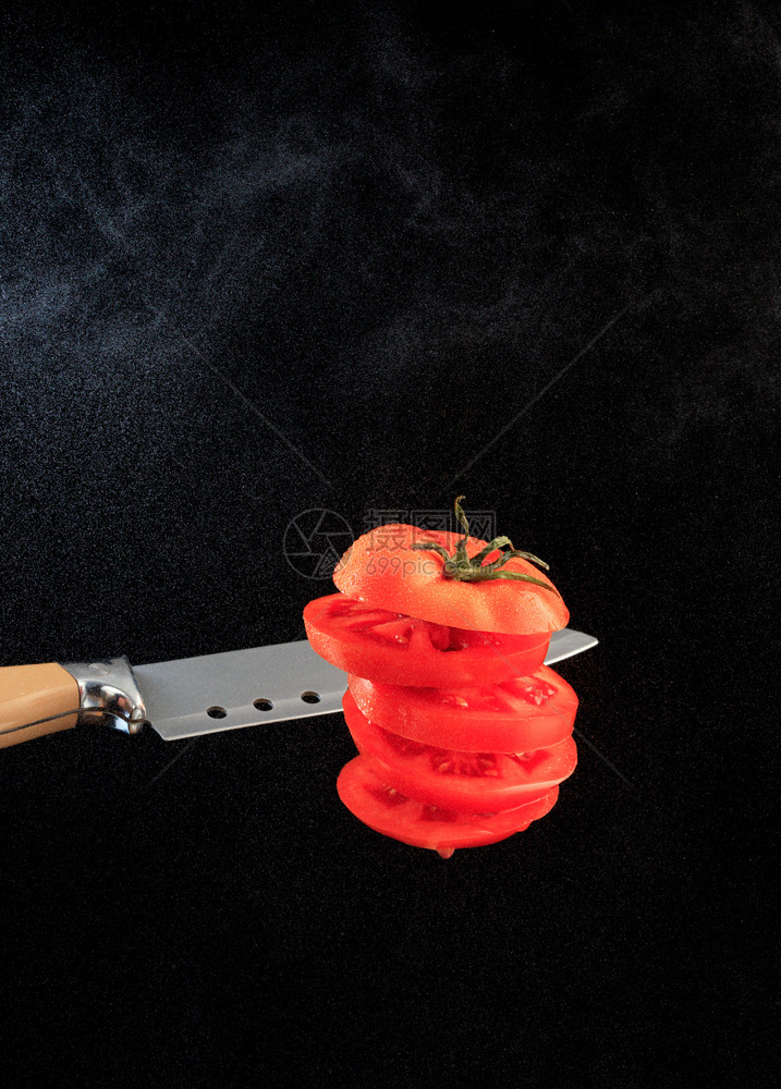 黑色背景光下水粉的红番茄和刀片垂直图象复制空间垂直图象在黑色背景上用水粉切开的番茄在黑色背景的水粉中冷冻新鲜的红色图片