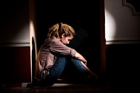 长发绺沮丧悲伤孤独不快乐悲哀的女孩坐在一个黑暗肮脏的房间里图片