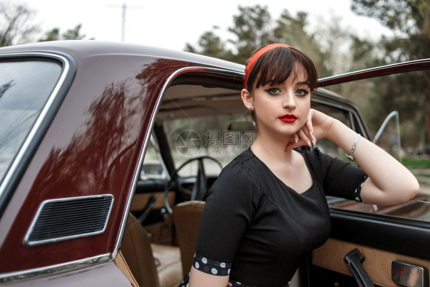 时髦的复古车轮身着黑色旧礼服的高加索年轻美女肖像在一辆旧车的小屋里摆姿样子图片