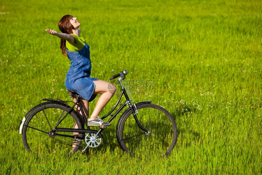 一种自由年轻女人骑着老旧自行车在绿色草地上放松喜悦图片