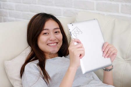现代的学习坐在沙发背景人与技术生活方式成人在线教育家工作时使用平板的年轻亚洲妇女在沙发环境中使用平板电话背景图片