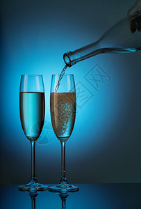 晚餐闪亮的食物两杯香槟从蓝色背景的瓶子里倒出两杯香槟从瓶子里倒出来图片