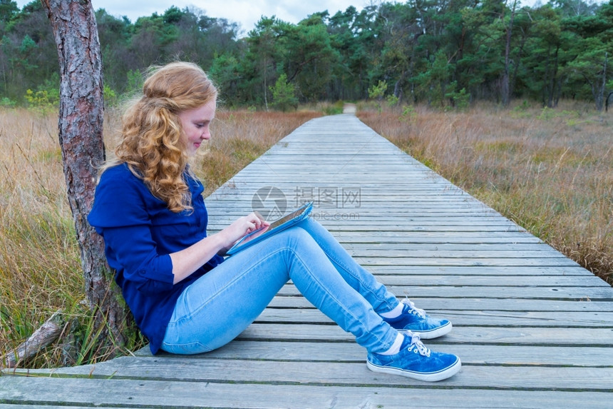 药片女士白种孩在天然木足道上使用平板电脑工作从事木制徒步活动自然图片