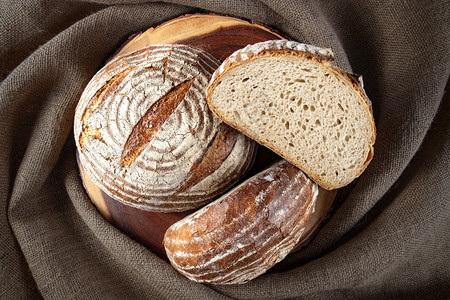 褐色面包将三个黑麦面包放在木头和花布上烘烤的小麦有机背景