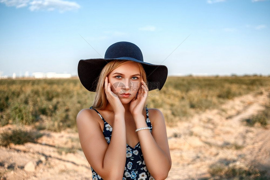 时髦的日落在葡萄园中摆放着一个戴黑帽子印有花粉的女红裙子和白的金发蓝眼睛女孩的近视肖像一种微笑图片