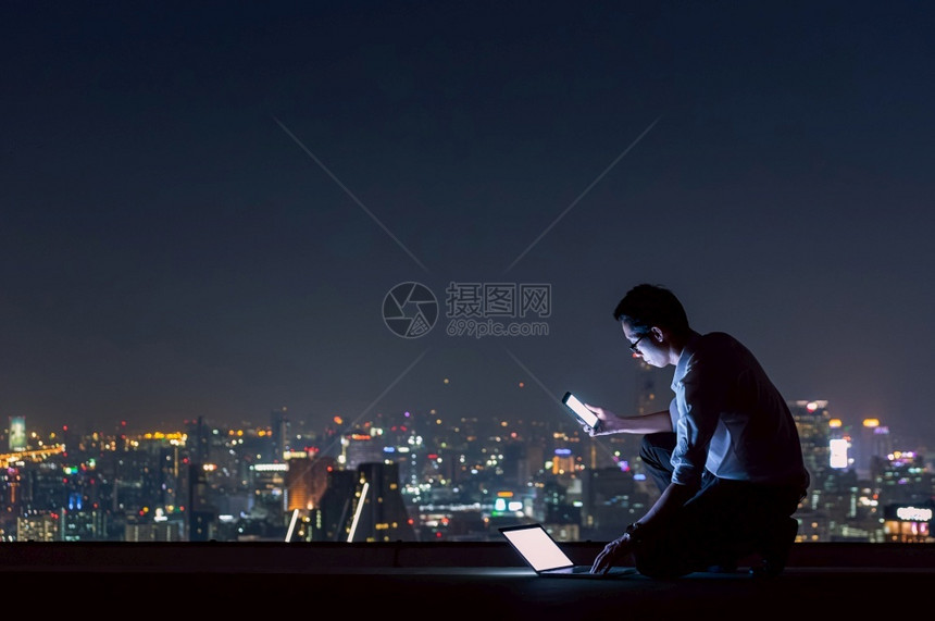 桌子时间采用使智能手机和笔记本电脑利用夜视城市的风景商业成功与技术概念在深夜工作a利用智能手机和膝上型计算以及夜间观察城市商业成图片