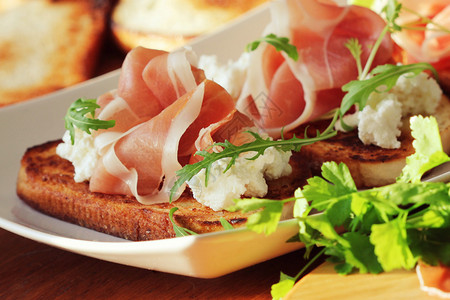 意大利语白盘上加乳清干酪意大利熏火腿芝麻菜的意式烤面包三明治地中海图片