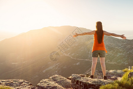 自由快乐的女士与敞开双臂停留在山悬崖边缘峰顶在日落光下出手图片