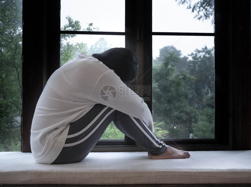 人们在家里下雨的一天坐在窗子上抱着膝盖的悲伤亚洲女人肖像锻炼伤心图片