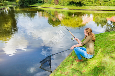 绿色水边带渔棍和着陆网的年轻天主教女青坐着季节图片