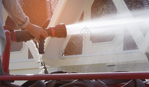 泰国橡胶橡胶在红色消防车上用喷水管灌龙头的男子手喷洒水用于清洁和减少公共场所照明光和背景模糊的空气灰尘问题管道打扫背景