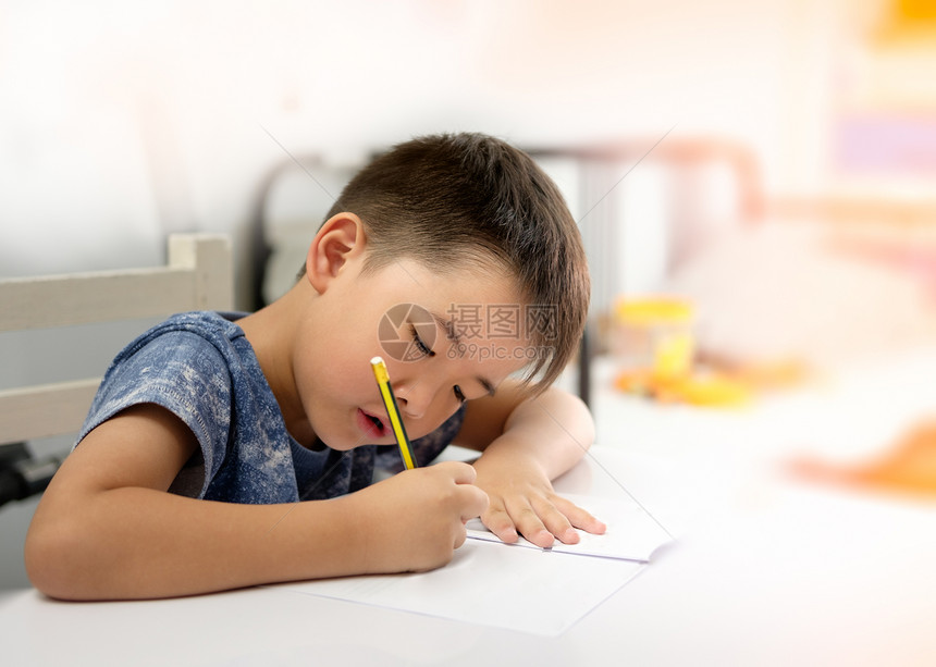 亚洲男孩正在做家庭作业和写与预期的脸装饰橙色灯光关注儿童铅笔白色的房间图片