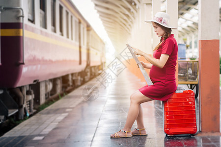 年轻的到达独自身着红色礼服并携带行李的亚洲妇女怀孕看火车站旅行图片