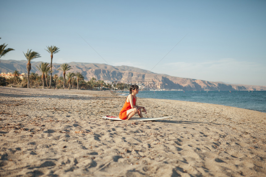 女人带着她冲浪板坐在沙滩上图片