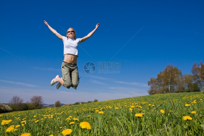 放松年轻的女子在花朵茂盛的草原上玩得开心跳图片