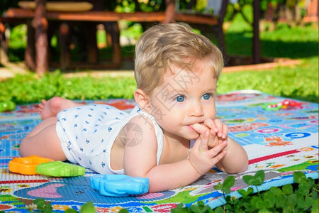 童年健康八个月大的漂亮男孩在花园里爬来去嘴用手指着甜的图片