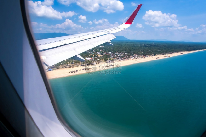 翅膀阳光明媚的夏日热带海滩空中景象飞机窗口风景岛屿村庄图片