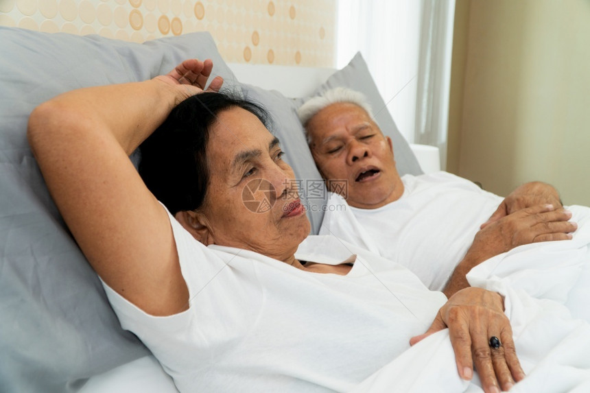 愤怒鼾年长的亚洲妇女在她丈夫身边睁开双眼躺在床上丈夫打呼噜制造噪音婚姻问题睡眠图片