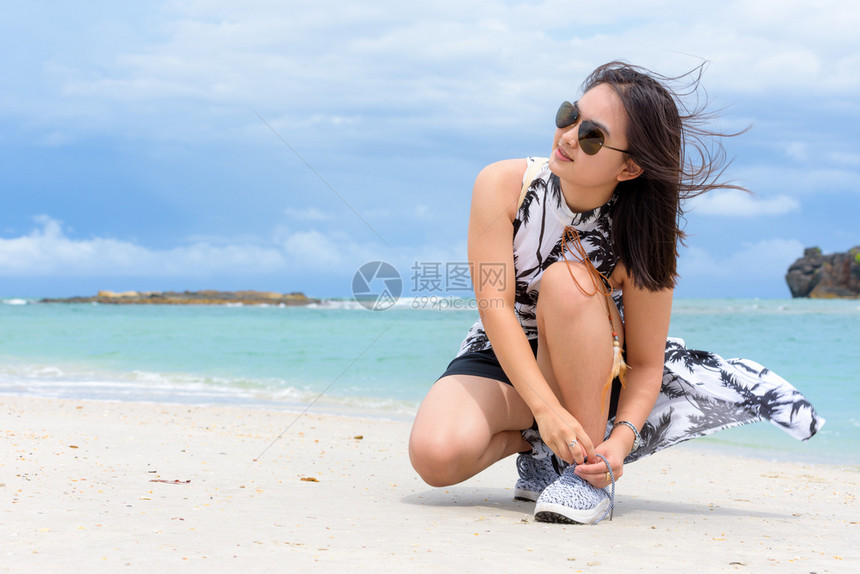 穿戴太阳眼镜的漂亮女游客在泰国沙滩渡暑假在Tarutao岛泰国Satun漫步时在靠近海边滩上搭紧绳子运动鞋并在海滩上搭绑绳子运动图片
