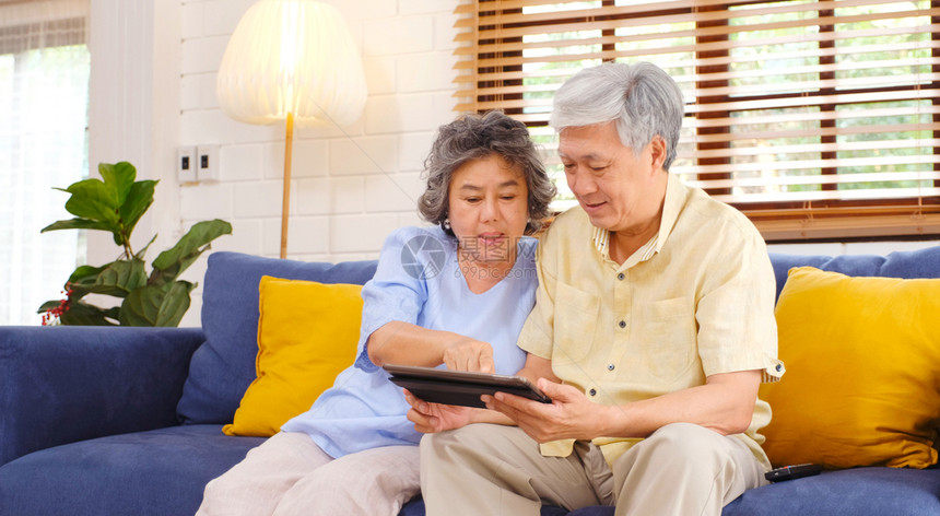 坐着退休使用数字平板电脑坐在沙发上的家庭客厅背景老年人和技术生活方式等沙地上快乐的老年同龄人情侣数字的图片