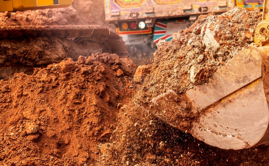经过行业通在建筑工地Bucket挖土掘挖掘机模糊的重型倾卸卡车挖掘机地面移动器挖掘车桶图片