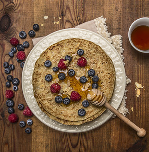 甜的早餐热美煎饼在白盘上餐巾纸配有蜂蜜和汤匙杏仁蓝莓和草还有一杯茶在生皮木本底顶端背景图片