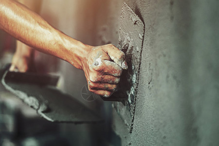 石膏硬件使固定工人们在建筑房屋墙上涂水泥的紧手背景图片