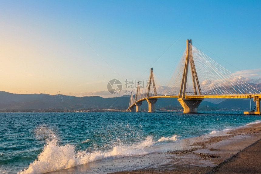 帕特雷海岸反里翁希腊科林斯湾的RionAntirion桥在混凝土路堤上喷洒冲浪日落灯桥和下的冲浪喷雾图片