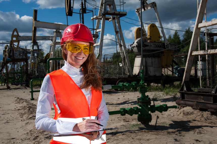 燃料商业穿戴红色头盔和工作服在油田上戴黄色眼镜的女工程师身着红头盔和工作服机械图片