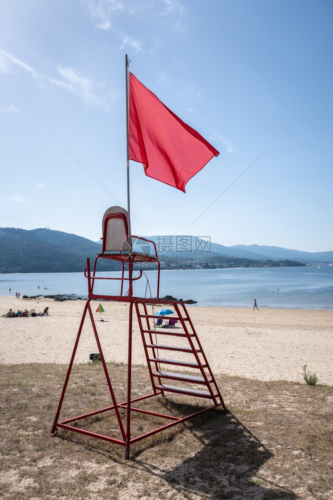 支撑西班牙加利亚海滩上没有游泳概念的红旗手挥舞着救生椅车站天图片
