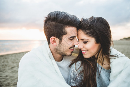 爱的男白毯覆盖坐在沙滩上情侣微笑背景图片