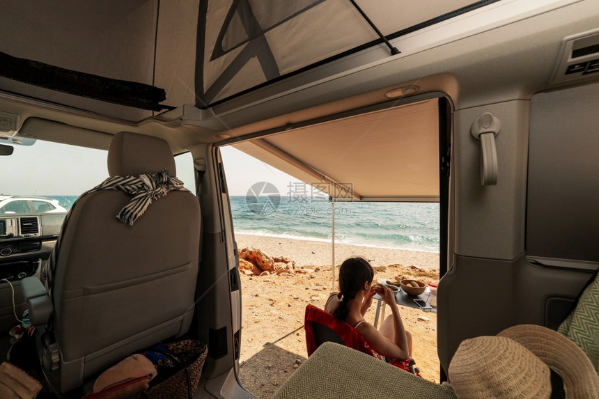 景观阳光人们一位年轻女子在她的大篷车里吃早餐观察海滩的美景图片