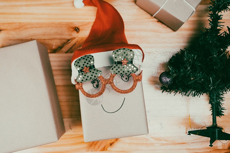 在室内圣诞老人手势礼品盒戴着圣诞眼镜帽在家里树附近的桌子上摆着笑脸新年快乐圣诞背景图片
