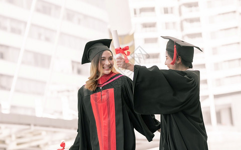 两位身穿红色学士服拿着毕业证书拍照的女学生青少年高清图片素材