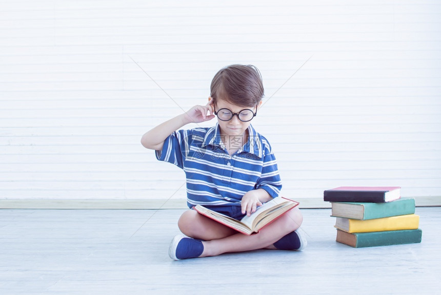 在阅读书本和思考教育概念时文化的书呆子小男孩肖像指点在家工作白种人图片
