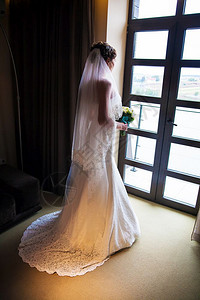 肖像穿着白色婚纱的美丽新娘站在卧室的里看着窗闺房魅力图片